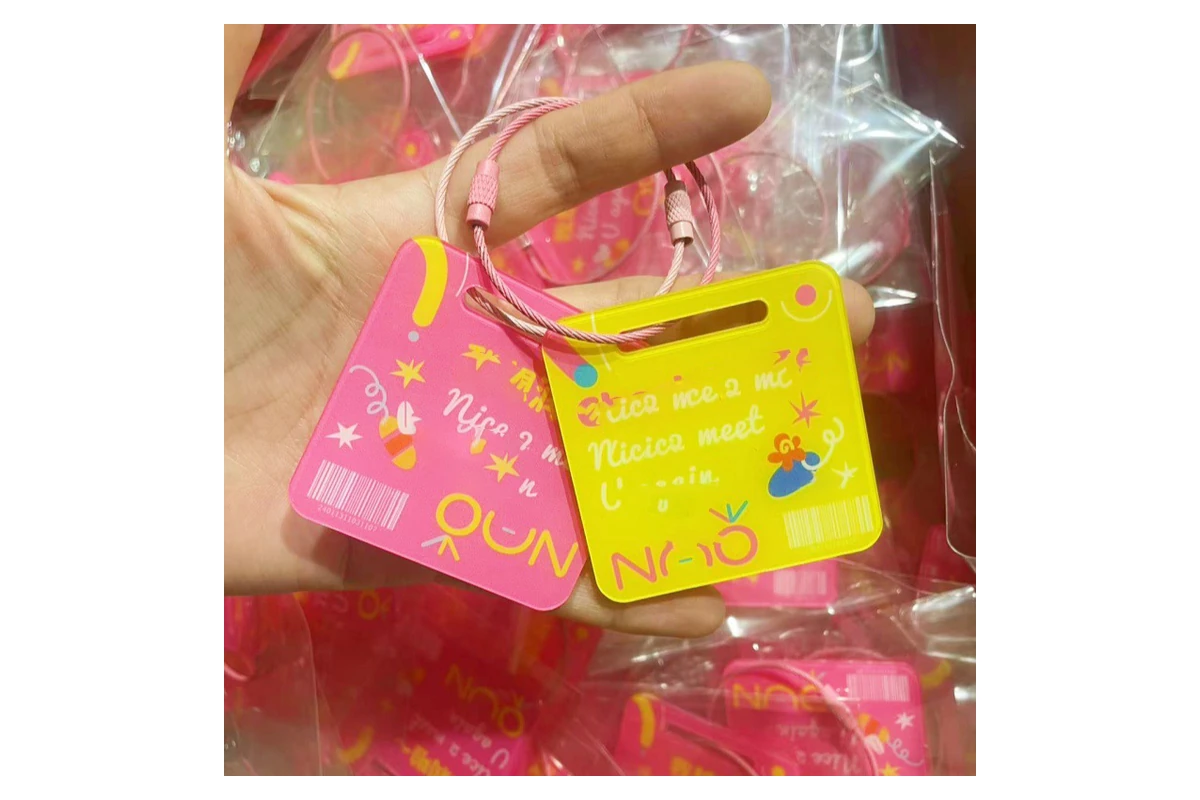 Pink and yellow printed acrylic tags held in a hand, with individually bagged tags behind them.