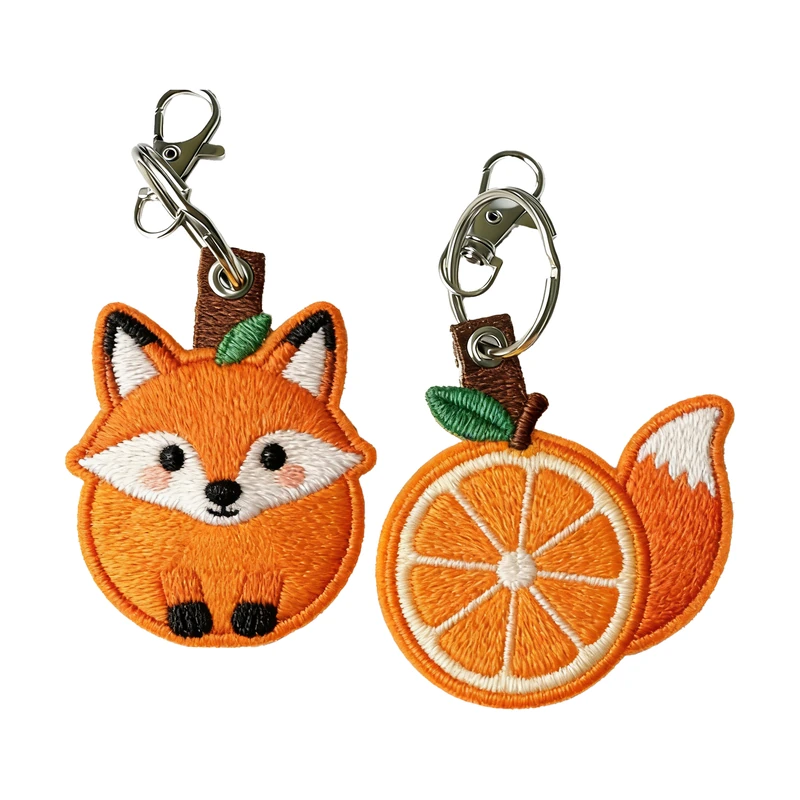 Fox and orange-slice shaped embroidered fabric keychains with metal clips.