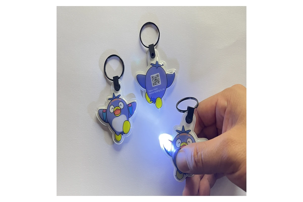 A bird-shaped keychain light being pressed to switch on its LED