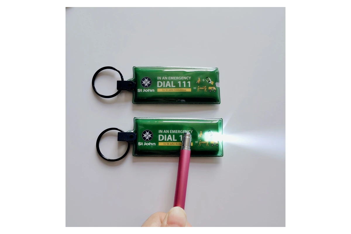 Two green keychain lights with printed labels and black rings, one illuminated.
