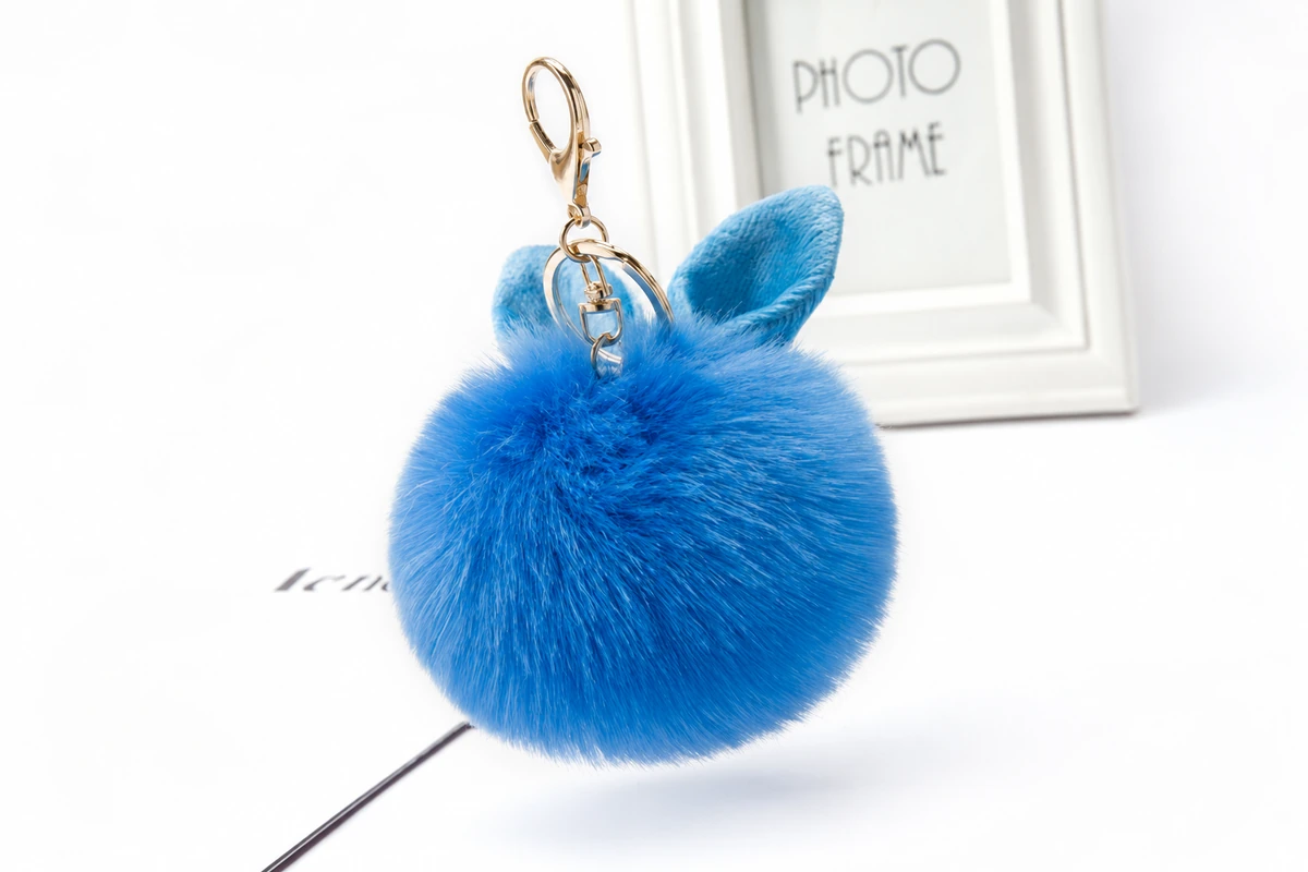 Blue plush pom-pom keychain with rabbit ears and a gold-colored clip.