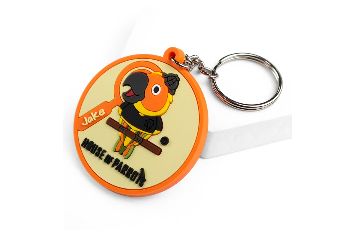 Round orange PVC keychain with a raised bird design and metal ring.
