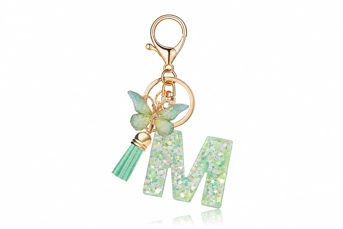 Green glitter-filled letter M keychain with a butterfly charm, tassel and gold-colored clip.