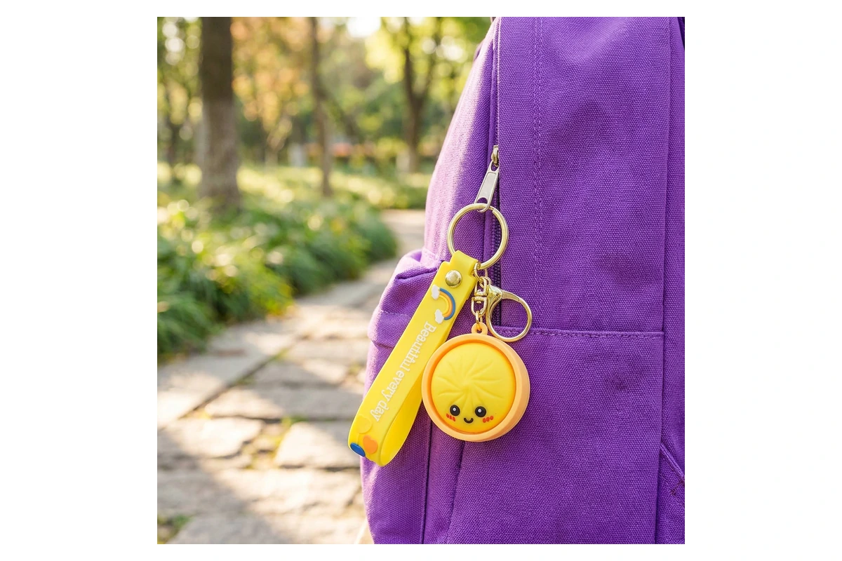 Yellow silicone character keychain and wrist strap attached to a purple backpack.