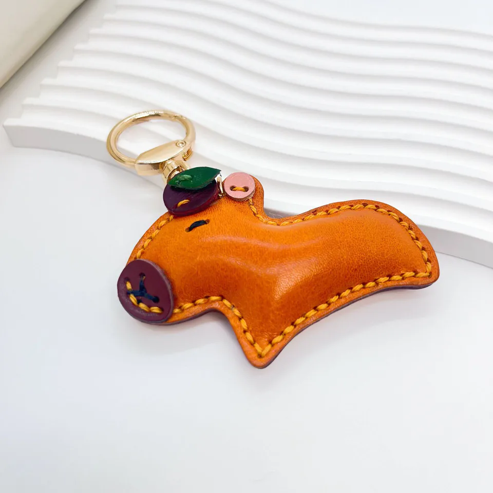Orange capybara charm with yellow stitching, a purple snout, and a gold-tone key ring.