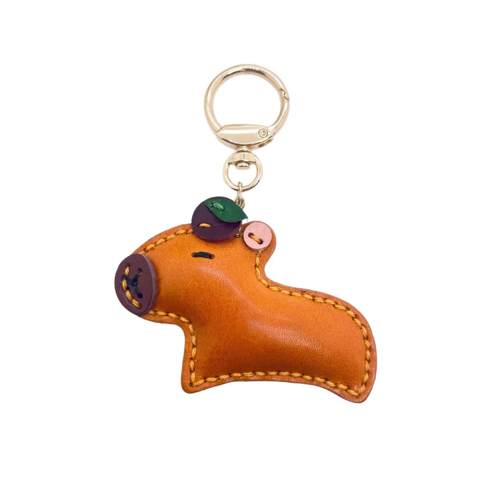 Orange capybara keychain with green and pink head details and yellow edge stitching.