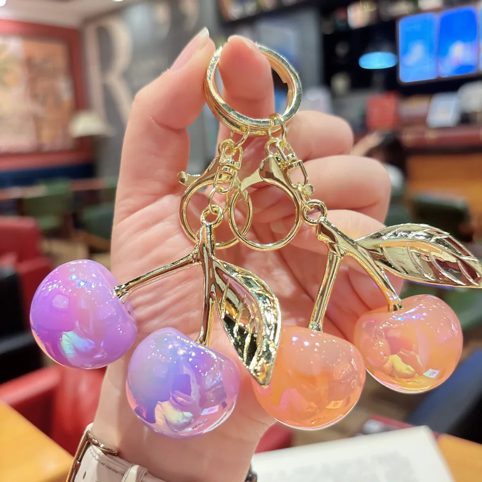 Purple and orange cherry-pair keychains with iridescent fruit charms and gold-tone leaves.