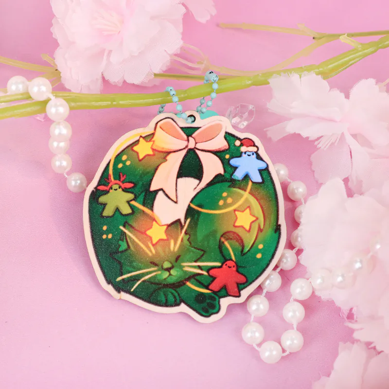 Green Christmas wreath keychain with a pink bow, yellow stars, and a blue bead chain.