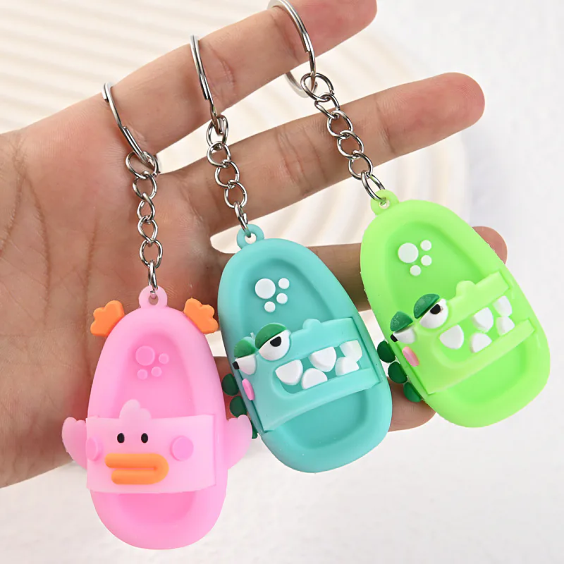 Green and teal crocodile slipper keychains beside a pink duck slipper keychain.