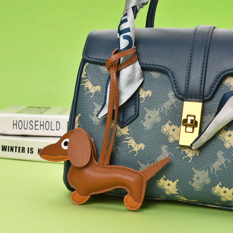 Brown dachshund charm hanging from a bag handle by a cord loop.