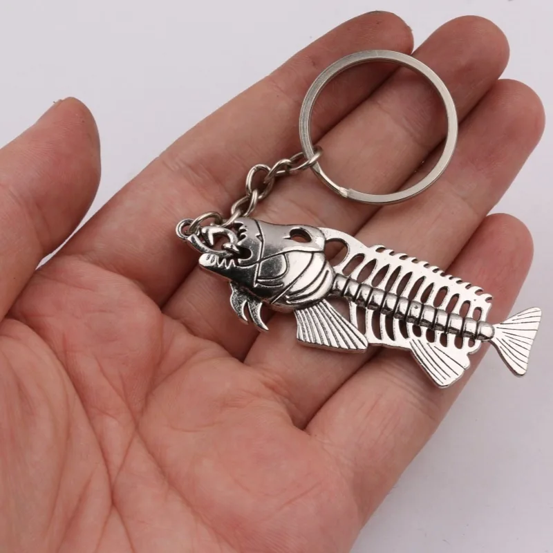 Silver-tone fish skeleton keychain with a round split ring resting in a palm.