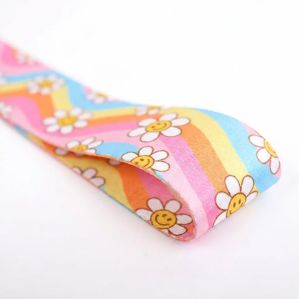 Close-up of a wristlet strap with white daisies, smiling yellow centers, and colorful stripes.