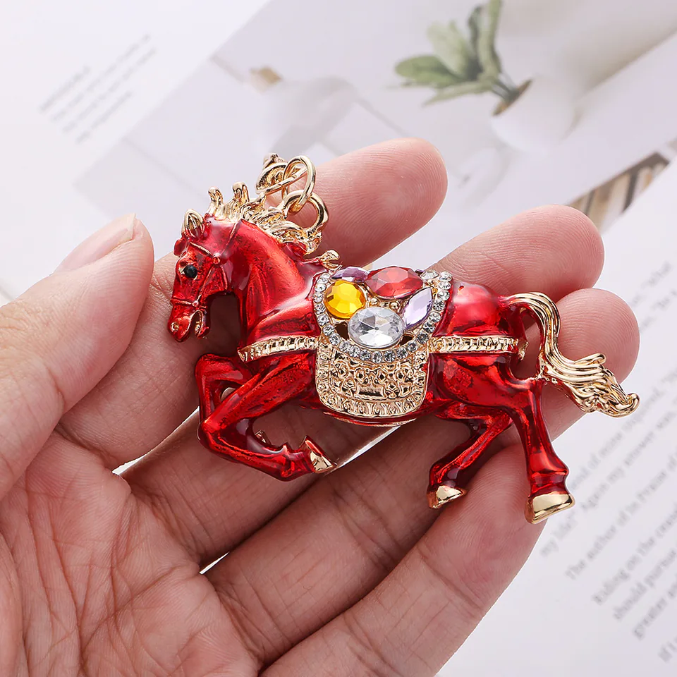 Close-up of a red horse charm showing colorful decorative stones and a gold-tone saddle.