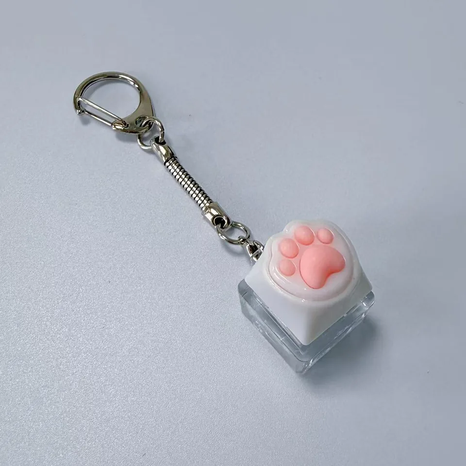 White keycap keychain with raised pink paw pads, a clear base, and a silver-tone clasp.