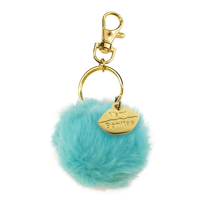 Turquoise pom-pom keychain with a gold-tone clasp and lip-shaped charm.