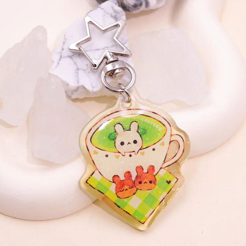 Teacup keychain depicting a white rabbit in green tea, with a silver-tone star clasp.