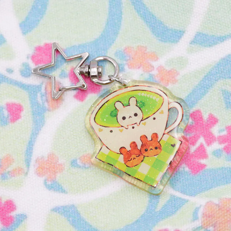 Teacup keychain with a white rabbit, two orange rabbits, and a green checkered base.