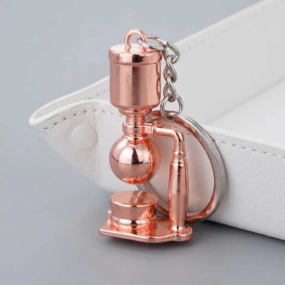 Side view of a rose-gold-tone siphon coffee maker keychain with a round chamber and support column.