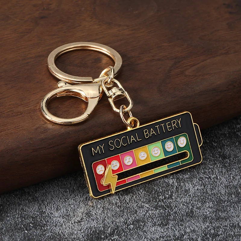 Black social battery keychain with gold-tone rings, a colored scale, and a lightning-bolt slider.