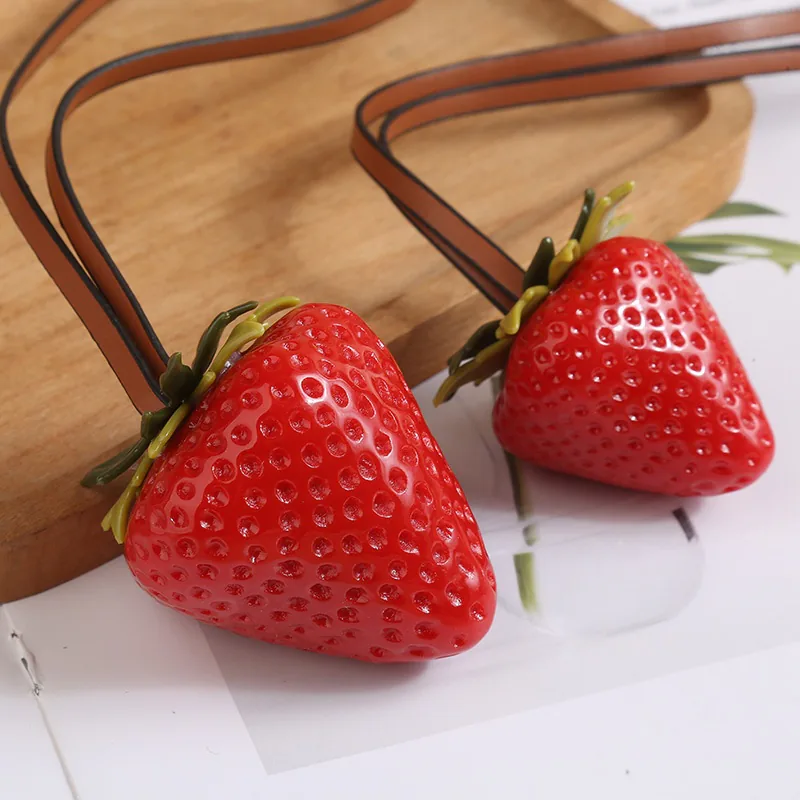 Two red strawberry charms with green leaves and brown hanging loops.