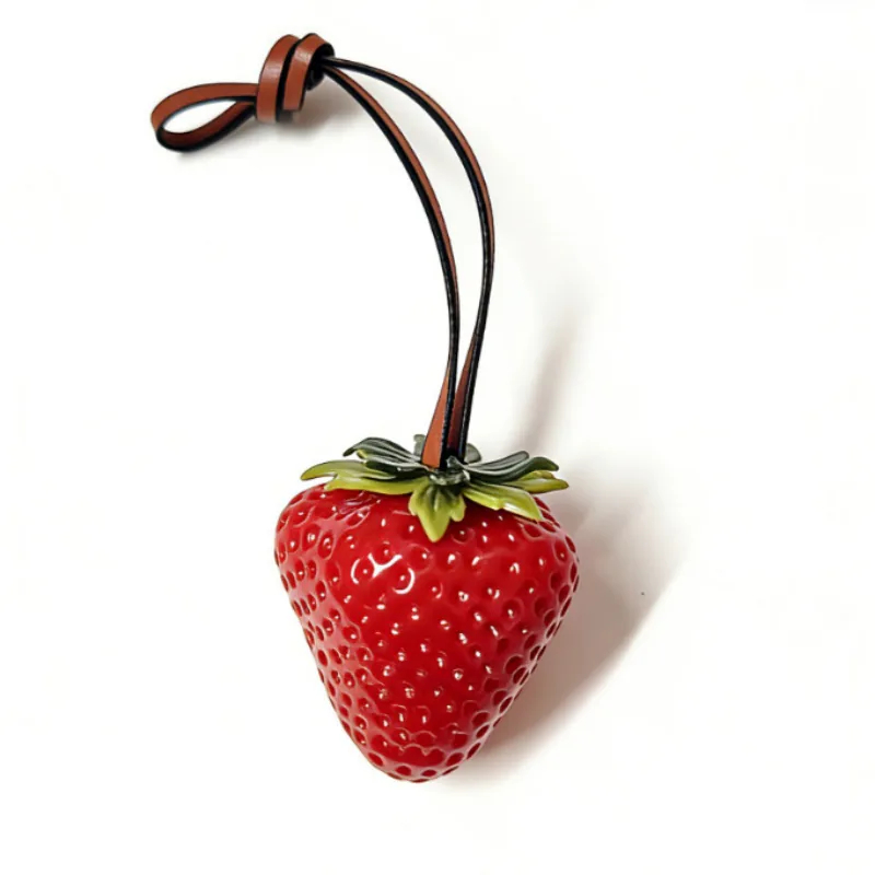 Red strawberry charm with green leaves and a knotted brown loop.